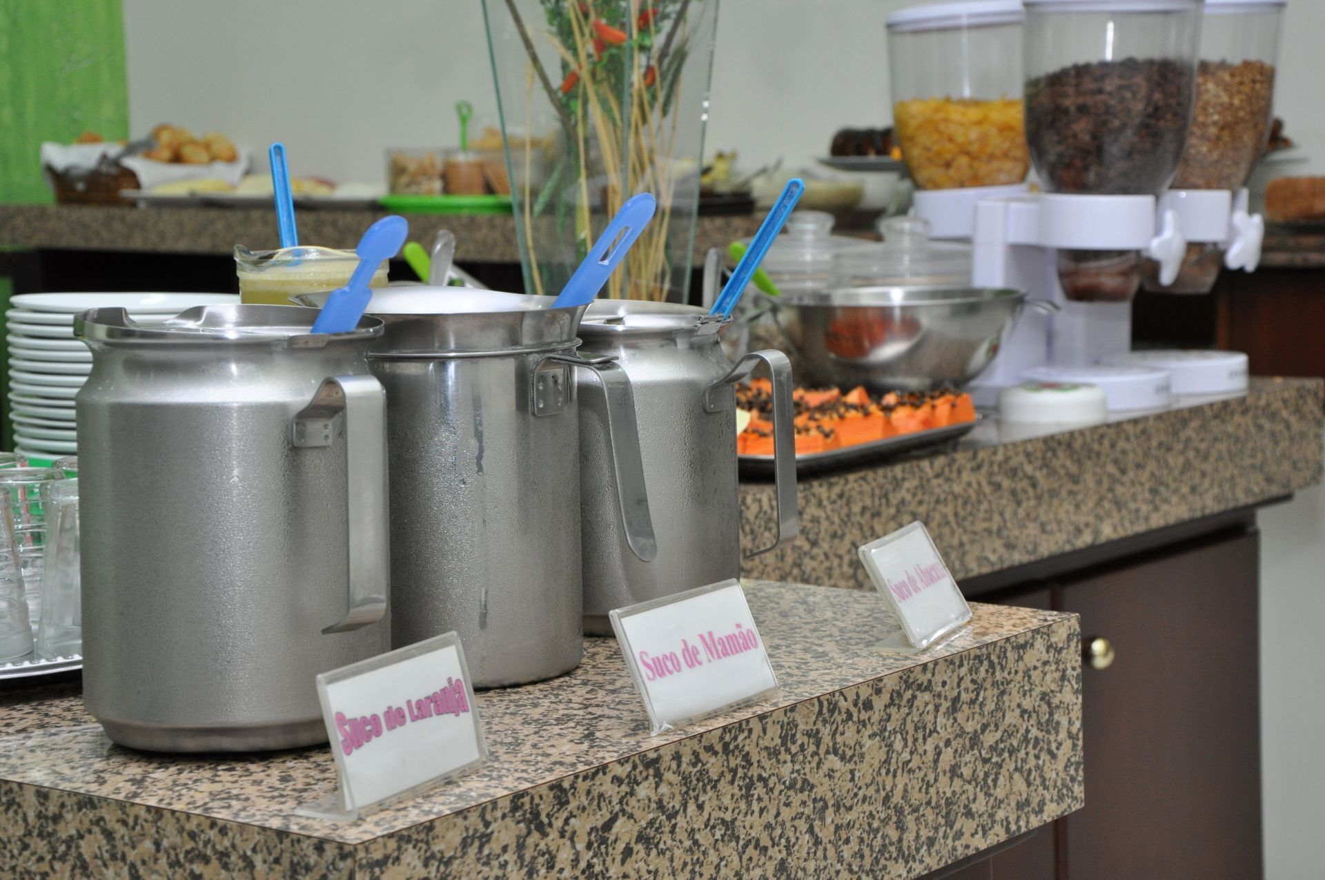 A buffet area with multiple stainless steel chafing dishes labeled 'Suco de Laranje' and 'Suco de Mamão'.