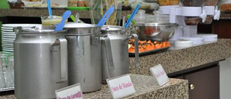 A buffet area with multiple stainless steel chafing dishes labeled 'Suco de Laranje' and 'Suco de Mamão'.