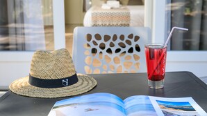 A straw hat, a glass of red beverage, and an open magazine on a table. - Joseph Charles (L'Île-Rousse)