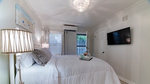 A bedroom with a bed, a lamp, a TV, and a window.