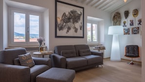 A modern living room with a grey sofa, a small round table with a bottle and glasses, and a large framed artwork on the wall. - Appartamento Matteotti (Florence)