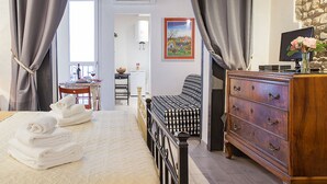 Une chambre à coucher avec un lit, une commode, un tableau et une fenêtre avec des rideaux.