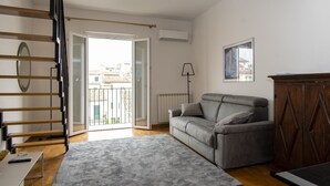 A living room with a grey sofa, a wooden cabinet, a grey rug, a floor lamp, and a staircase. - Apollonia Apartment (Florence)