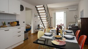 A modern kitchen with white cabinets, a dining area with a black table, and a staircase leading to another level. - Apollonia Apartment (Florence)