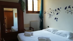 A hotel room with a bed, a radiator, a window with curtains, and a mirror reflecting the room. - Appartamento Ruote (Florence)