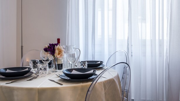 Ein Esstisch gedeckt mit schwarzen Tellern, klaren Gläsern und einer Vase mit violetten Blumen.