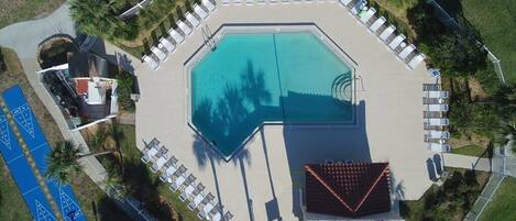 An octagonal pool surrounded by lounge chairs and a small building with a red roof.