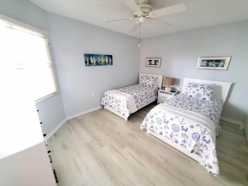 A bedroom with two beds, a ceiling fan, and a window with blinds.
