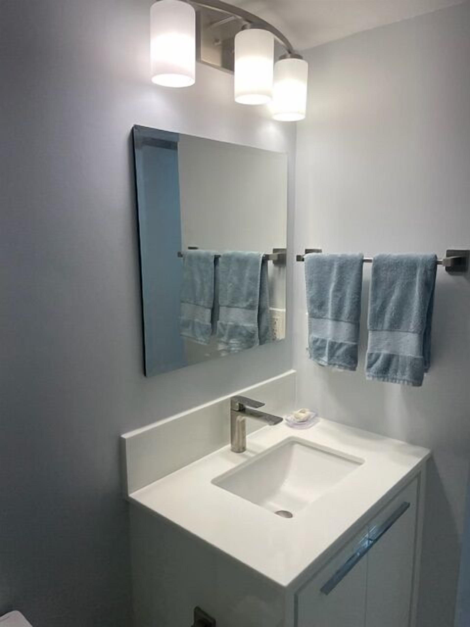 A modern bathroom with a white sink, a large mirror, and two towels hanging on a towel rack.