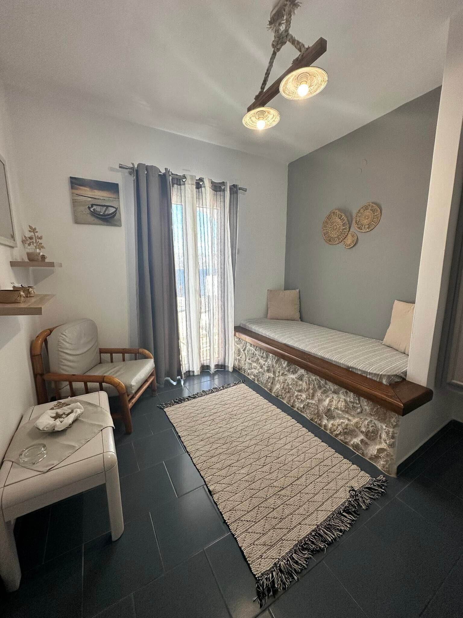 Una habitación pequeña con cama, una silla, una mesita y ventana con cortinas.