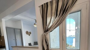 Un dormitorio con cama, ventana con cortinas, espejo y vista al mar.