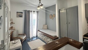 Una habitación compacta con una cama, una pequeña zona de estar, un mostrador de madera y un ventilador de techo.