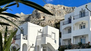 Un edificio blanco con balcones y arcos, situado frente a una ladera rocosa.