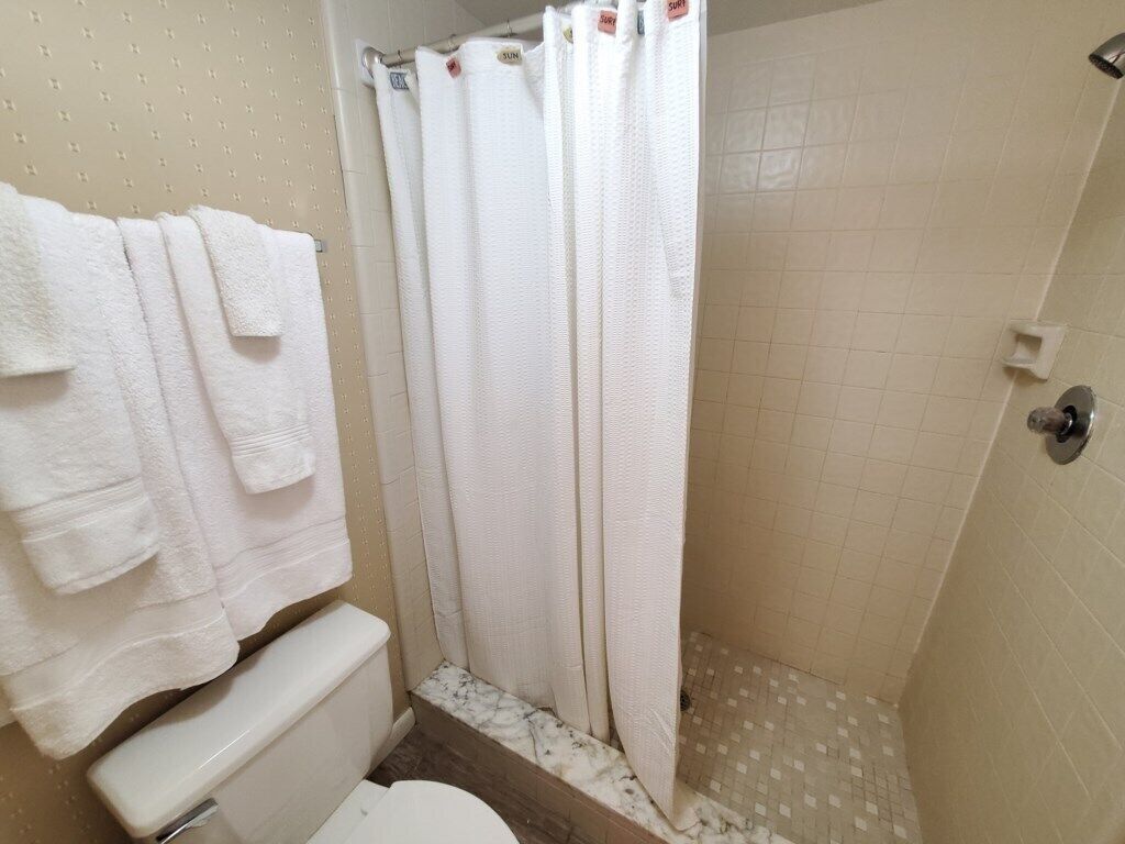 A bathroom with a toilet, a shower with a white curtain, and a towel rack with white towels.