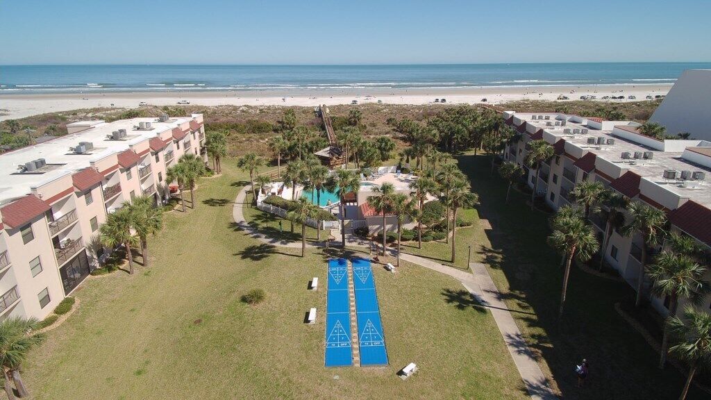 A hotel with a pool area, surrounded by palm trees and a beach view.