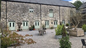 A stone building with multiple windows and doors, a gravel courtyard, and outdoor seating. - Four bedroom stone barn conversion near Dartmoor and Devon beaches (Newton Abbot)