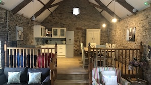 A rustic kitchen with stone walls, wooden beams, and basic amenities including a microwave, refrigerator, and cabinets. - Four bedroom stone barn conversion near Dartmoor and Devon beaches (Newton Abbot)