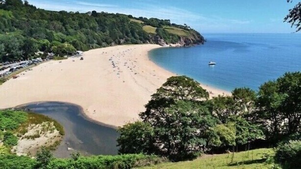 A beach with a curved shoreline, a boat in the water, and dense greenery in the background. - Four bedroom stone barn conversion near Dartmoor and Devon beaches (Newton Abbot)