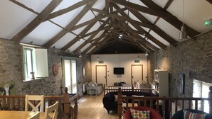 A rustic interior with exposed wooden beams, a wooden dining table with chairs, a red armchair, and a sofa. - Four bedroom stone barn conversion near Dartmoor and Devon beaches (Newton Abbot)