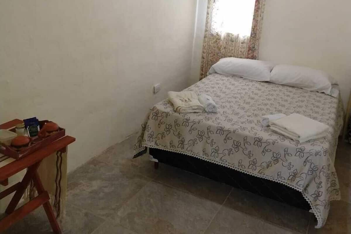 A bedroom with a bed, a wooden desk, a wall-mounted air conditioner, and a ceiling light fixture.