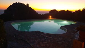 Una piscina con vistas al atardecer, rodeada de rocas y vegetación.
