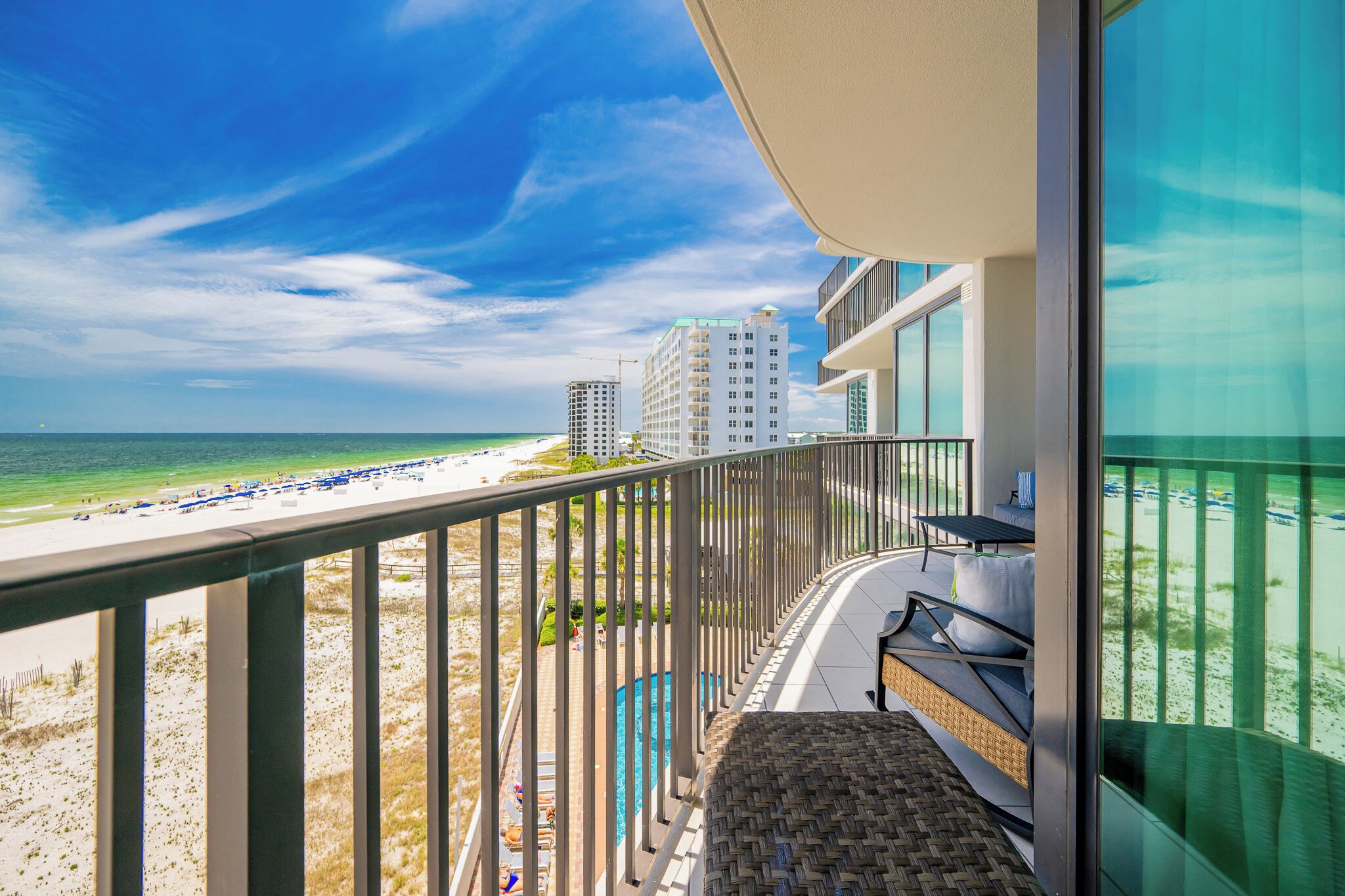A balcony with a view of the beach and ocean, a pool, and a seating area with a view.