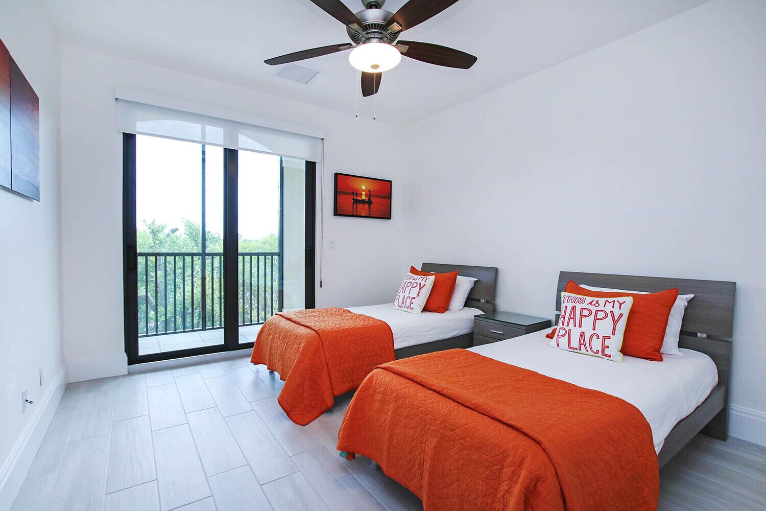 Een moderne slaapkamer met twee bedden, een plafondventilator en een grote schuifdeur naar een balkon.