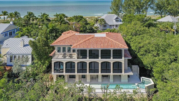 A large two-story house with a swimming pool, surrounded by lush greenery and a view of the ocean. - Bayfront Luxury Home with Private Pool, Spa & Panoramic Views (Captiva)