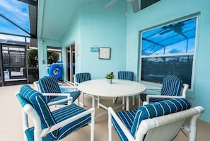 A covered patio with a round table and striped chairs, a small plant, and a window with a view. - Family 4BR Pool  Near Disney (Kissimmee)