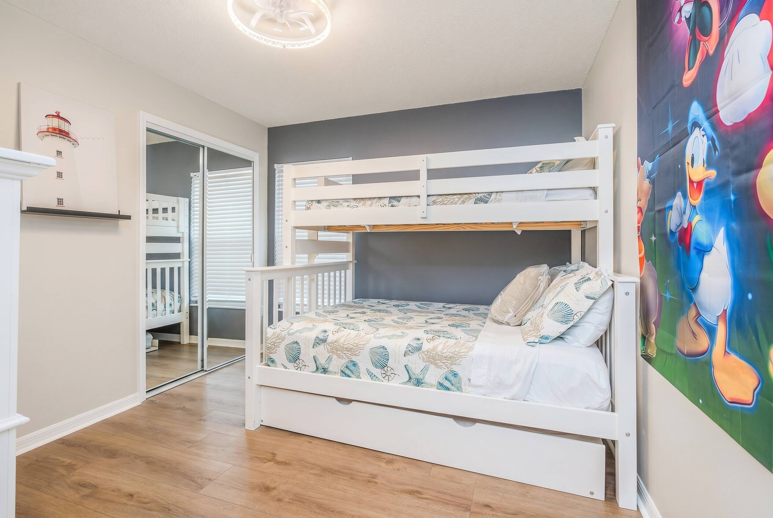 A bunk bed with a patterned bedspread, a white crib, and a wall with a cartoon character mural.