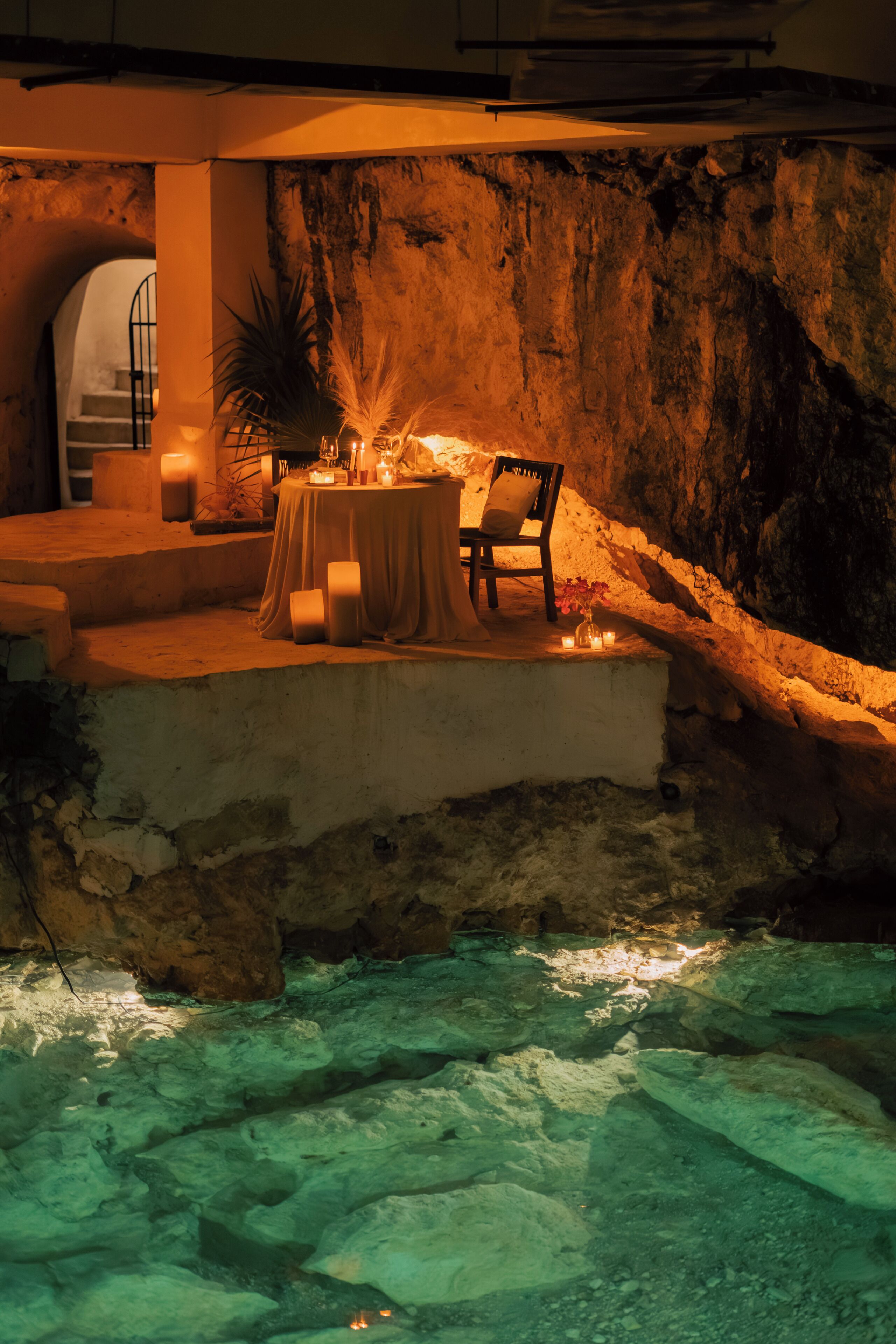 A table set up on a stone ledge with candles, a chair, and a potted plant.