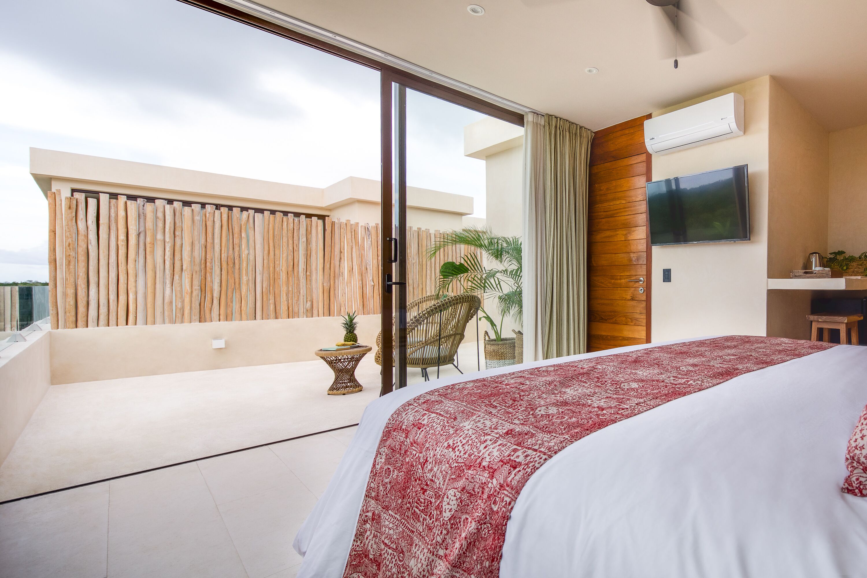 Una habitación de hotel moderna con una cama grande, un ventanal corredero que da a un balcón, un televisor de pantalla plana en la pared y un ventilador de techo.