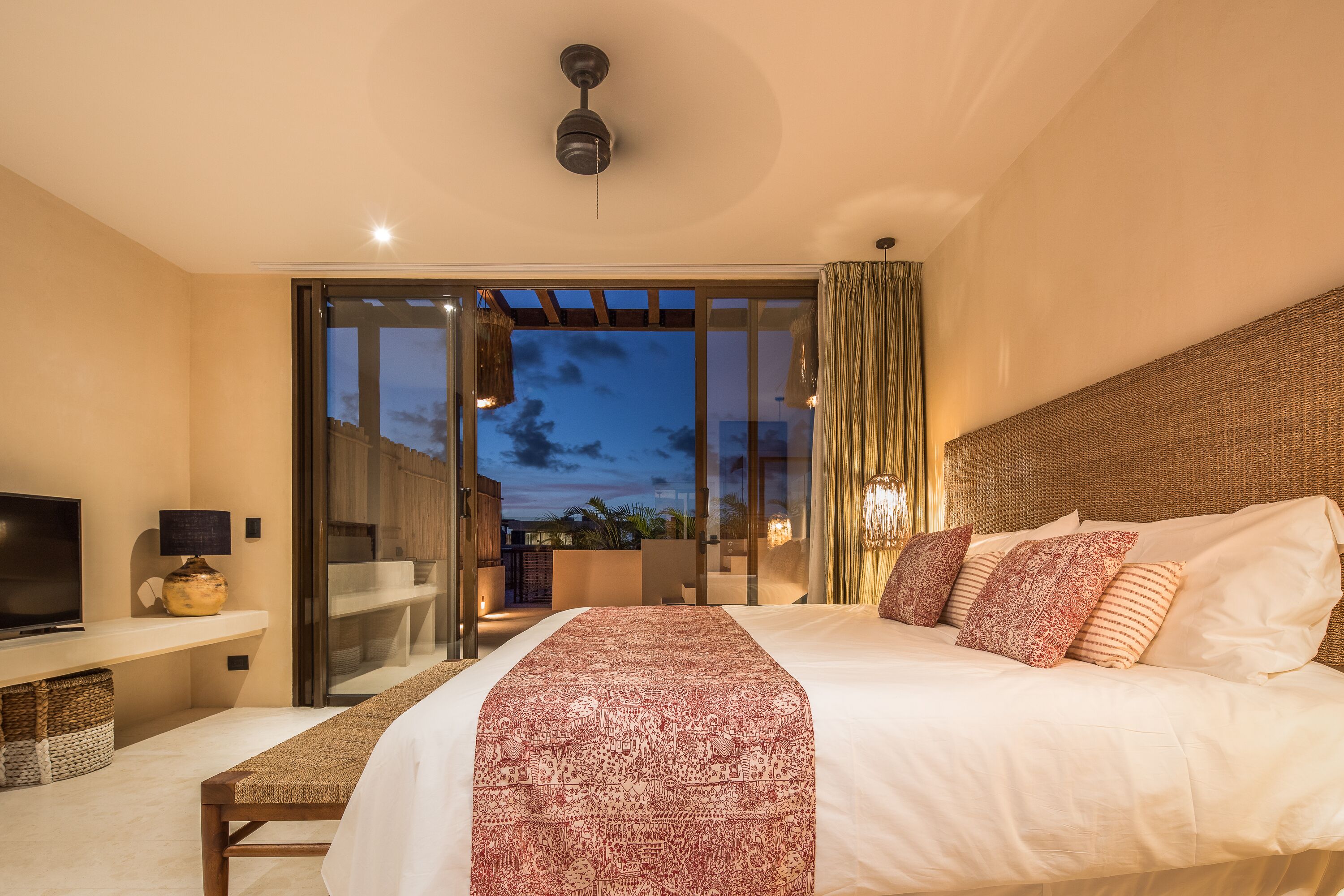 Habitación de hotel moderna con una cama grande, televisión y balcón con vista al cielo nocturno.