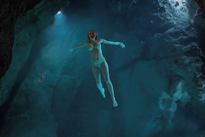 A person swimming in a cave with rocky walls and a light source.