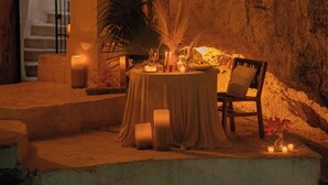 Una mesa colocada sobre una plataforma de piedra, con velas, una planta en maceta y una silla.