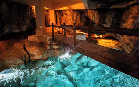 A cave-like interior with a wooden bridge over a pool, stone walls, and a warm light source.