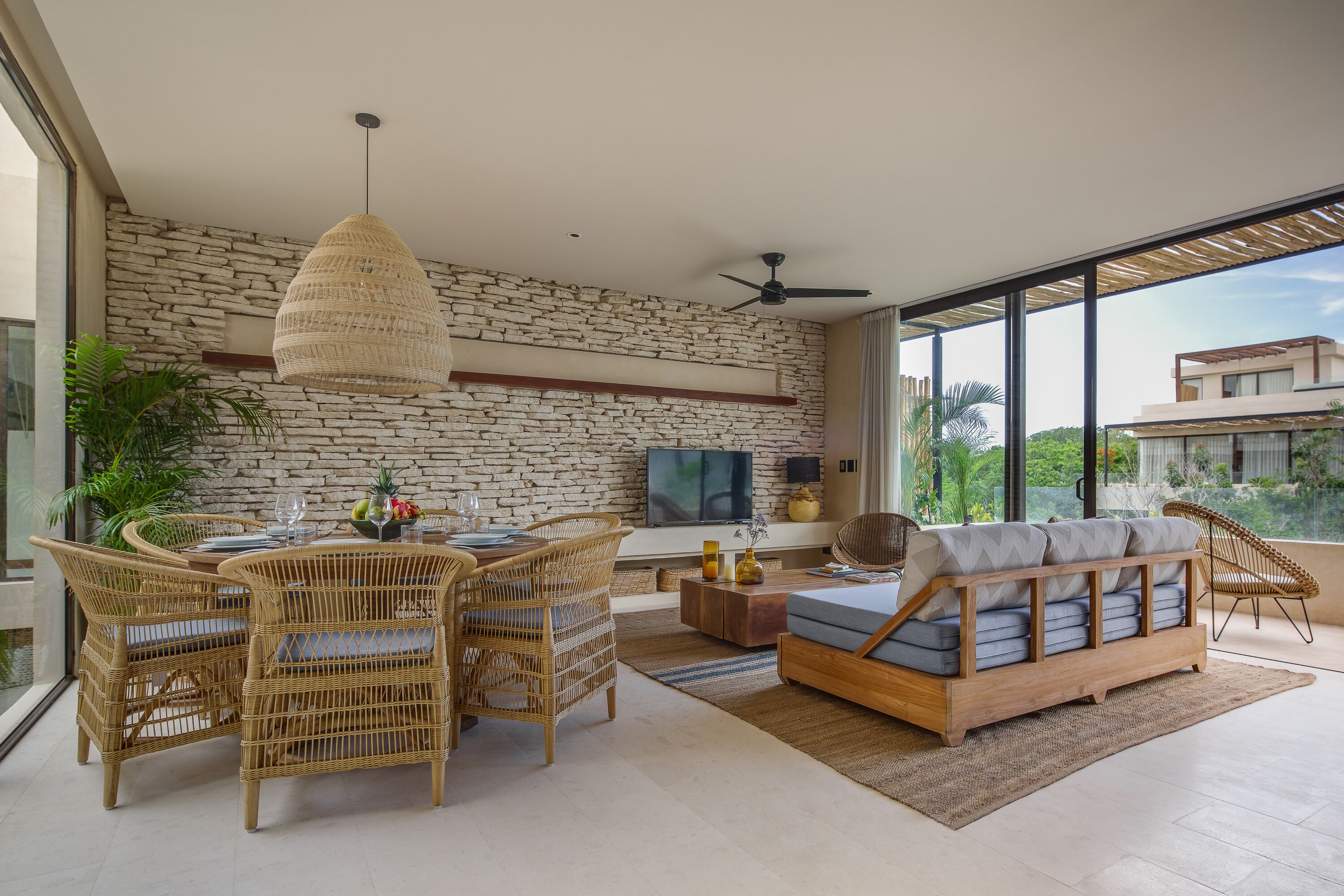 Una sala de estar moderna con pared de piedra, muebles de mimbre, un televisor de pantalla plana y un ventanal con vistas a la ciudad.