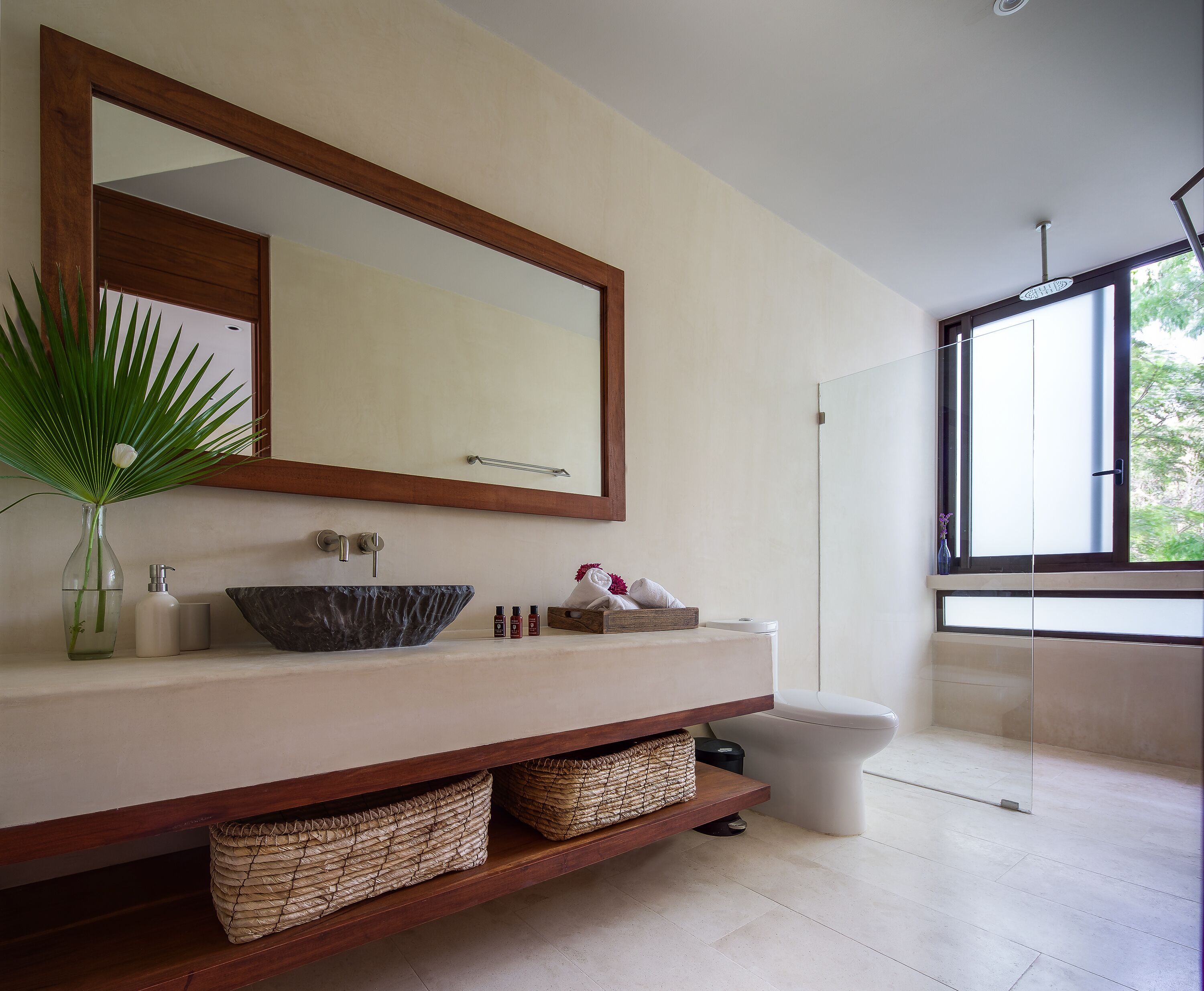 Un baño moderno con un espejo grande, un recipiente con una planta, un lavamanos de mármol y un inodoro.