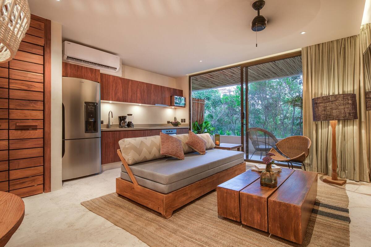 A modern living room with a sofa, coffee table, and a kitchen area with a refrigerator and microwave.