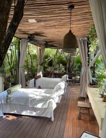 Una terraza de madera con una cama, cortinas e iluminación colgante.