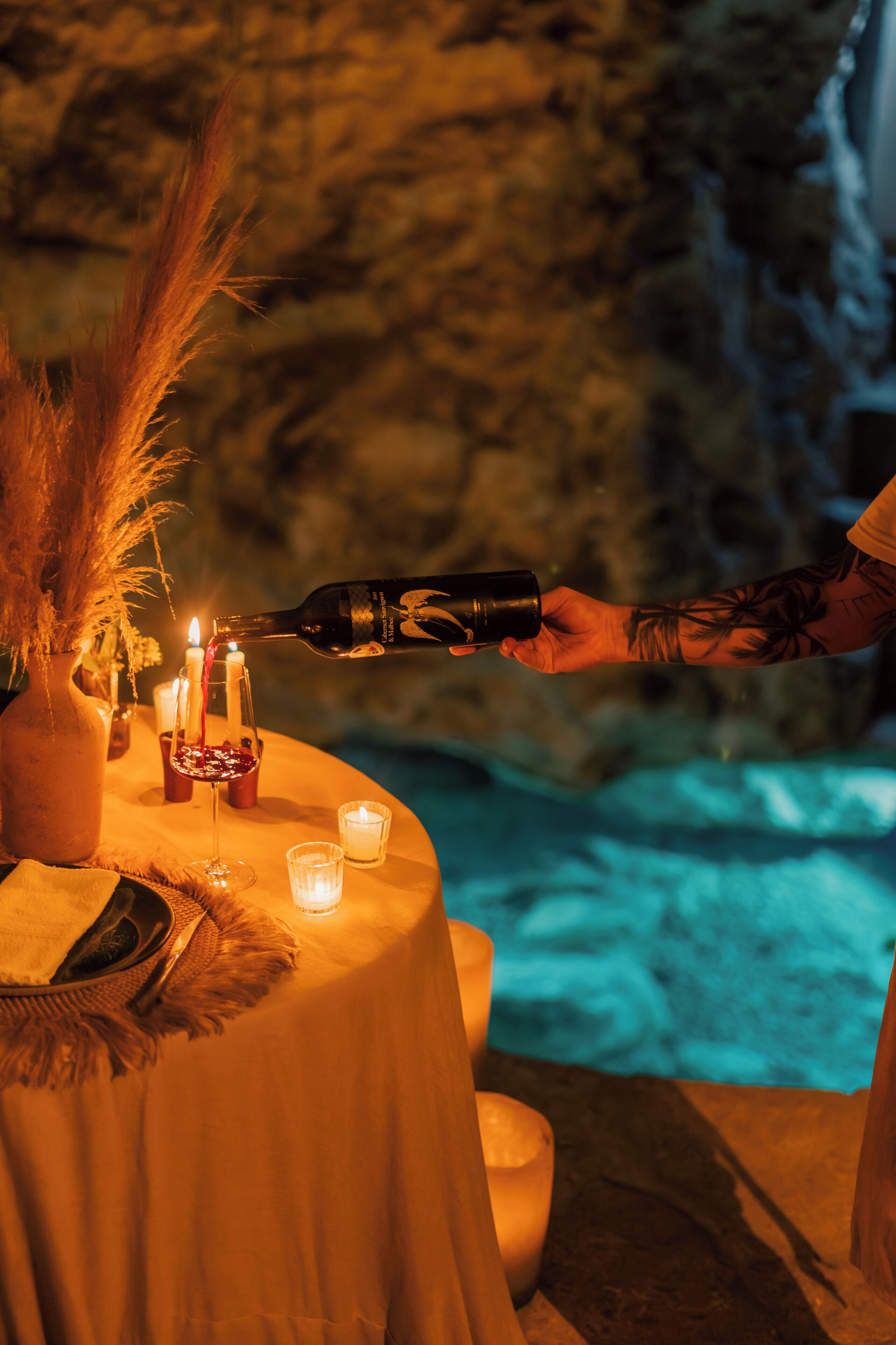 A table set with candles, a bottle of wine, and a vase of dried plants.