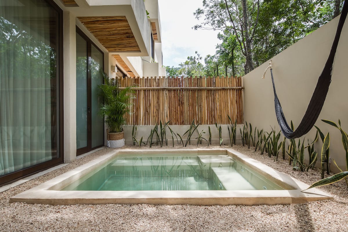 A rectangular pool with a pebble border, surrounded by a bamboo fence, and a hammock hanging on the right.