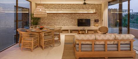 A modern living room with a stone wall, a flat-screen TV, wicker furniture, and a large window.