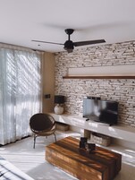 Una sala de estar moderna con pared de piedra, un televisor de pantalla plana, un ventilador de techo y una mesa de centro de madera.