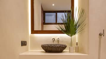Une salle de bain avec un grand miroir, un lavabo en pierre et deux paniers en osier placés sur des étagères.