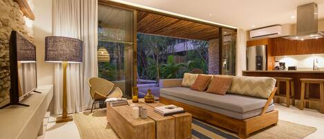 A modern living room with a sofa, coffee table, and a view of a garden through large windows.