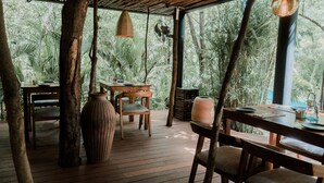 A wooden deck with a table and chairs, surrounded by tropical foliage.