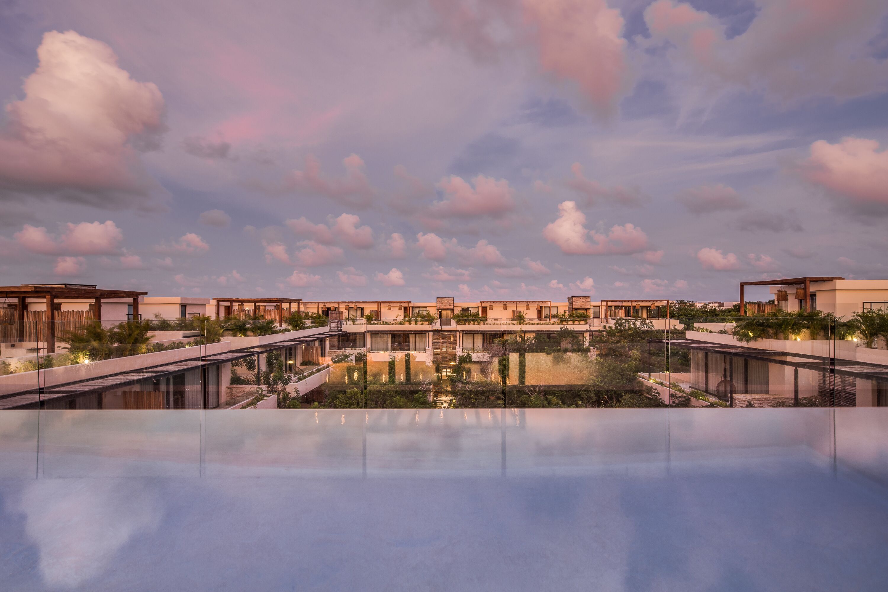 A modern resort with a rooftop pool, reflecting the sky and clouds.
