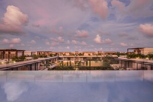 Un complexe hôtelier moderne doté d’une piscine sur le toit, qui reflète le ciel et les nuages.