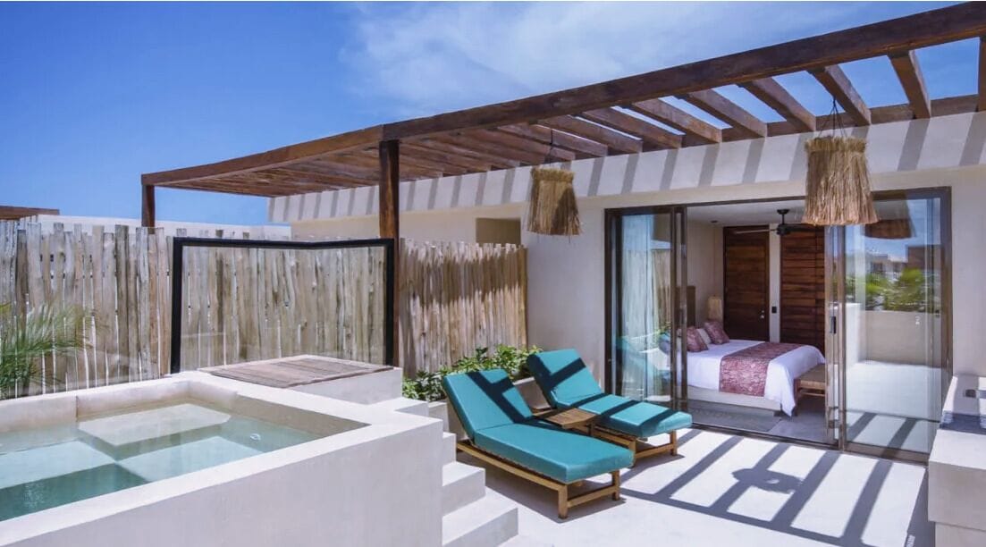 Un espacio exterior moderno con jacuzzi, sillones de descanso y un dormitorio con paredes de vidrio.